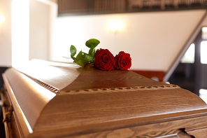 funeral and mourning concept - red rose flowers on wooden coffin in church