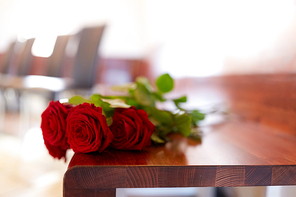 funeral and mourning concept - red roses on bench in church