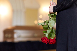 people and mourning concept - close up of woman with red roses and coffin at funeral in church