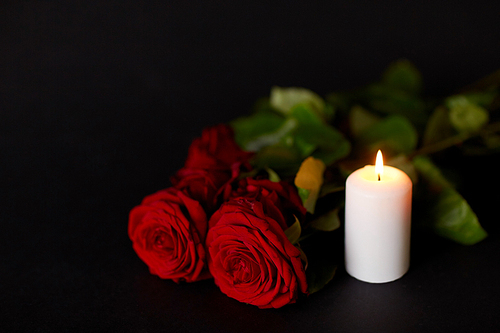 funeral and mourning concept - red roses and burning candle over black background