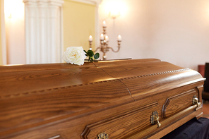 funeral and mourning concept - white rose flower on wooden coffin at funeral in church