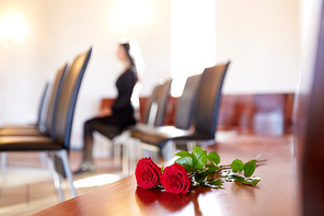 people and mourning concept - red roses and woman crying at funeral in church