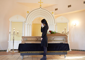 burial, people and mourning concept - sad woman with coffin at funeral in orthodox church