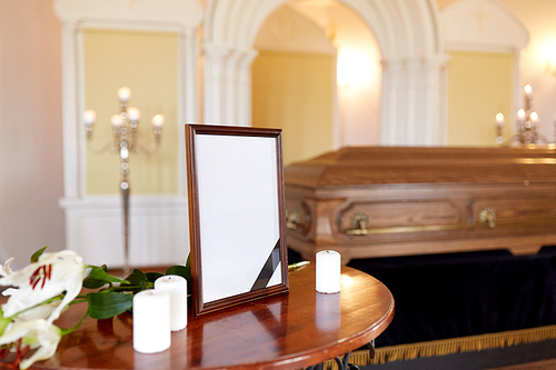 funeral and mourning concept - photo frame with black ribbon, candles and coffin at church