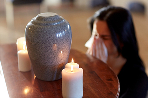 cremation, people and mourning concept - woman with wipe and cinerary urn crying at funeral in church