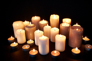 mourning and commemoration concept - candles burning in darkness over black background