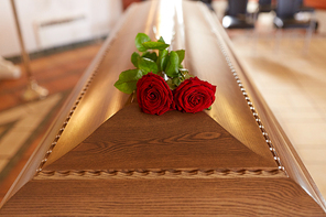 funeral and mourning concept - red rose flowers on wooden coffin in church