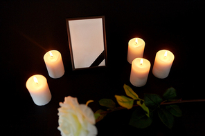 funeral and mourning concept - photo frame with black ribbon, flower and burning candles in darkness
