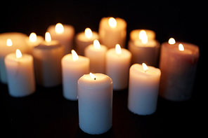 mourning and commemoration concept - candles burning in darkness over black background