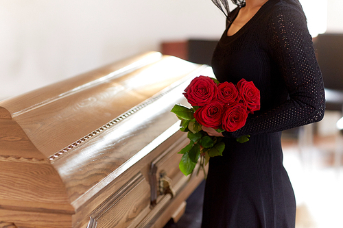 people and mourning concept - woman with red roses and coffin at funeral in church