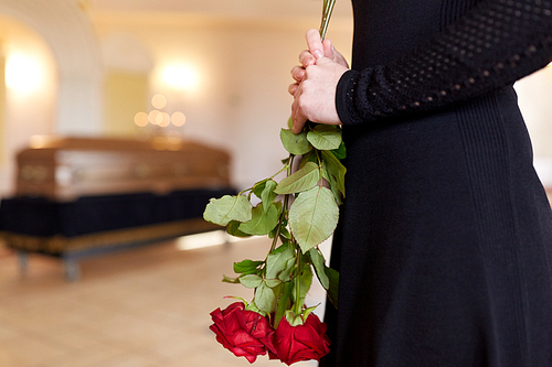 people and mourning concept - close up of woman with red roses and coffin at funeral in church