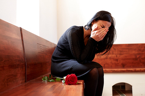 people, grief and mourning concept - crying woman with red rose sitting on bench at funeral in church