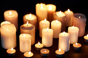 mourning and commemoration concept - candles burning in darkness over black background