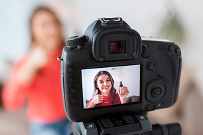 blogging, technology, videoblog, makeup and people concept - happy smiling woman or beauty . with foundation and camera recording tutorial video at home and showing thumbs up