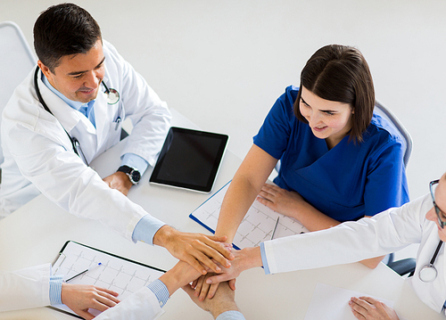 medicine, healthcare and cardiology concept - group of doctors with cardiograms, clipboards and tablet pc computer holding hands together at hospital