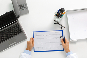 medicine, healthcare, cardiology and people concept - doctor hands with cardiogram on clipboard and laptop computer sitting at table in clinic