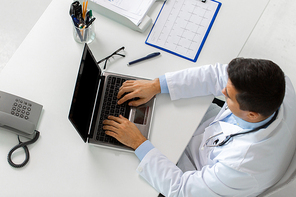 medicine, healthcare and people concept - doctor with cardiogram on clipboard typing on laptop computer sitting at table in clinic