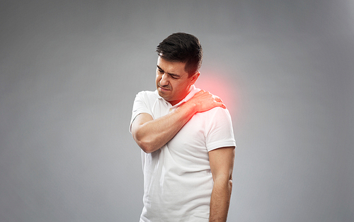 people, healthcare and problem concept - unhappy man suffering from pain in shoulder over gray background