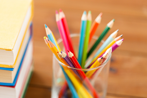 education, art, drawing, creativity and object concept - close up of crayons or color pencils and books on wooden table