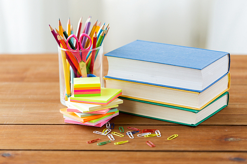 education, school supplies and object concept - close up of stand or glass with writing tools and book with scissors on wooden table