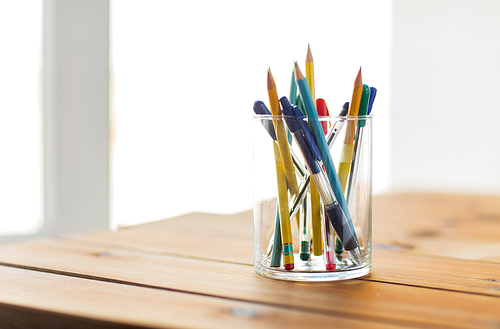 education, office supply, writing tools and object concept - close up of stand or glass with pens and pencils on wooden table