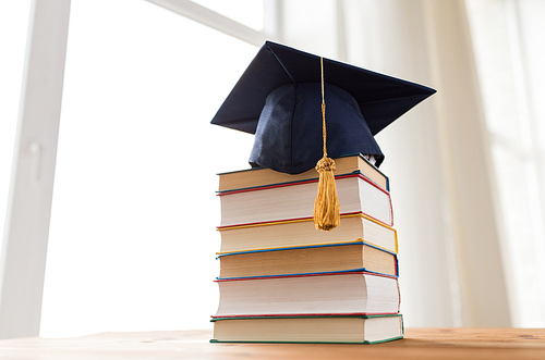 education, school, graduation and knowledge concept - close up of books and mortarboard on wooden table