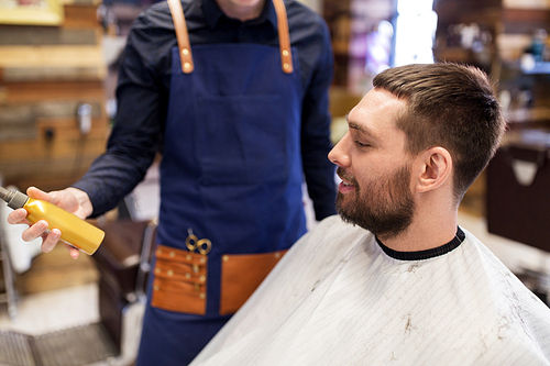 grooming, hairdressing and people concept - hairstylist showing hair styling spray to male customer at barbershop