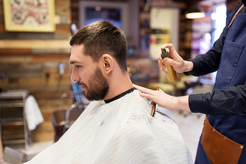 grooming, hairdressing and people concept - hairstylist applying hair styling spray to male customer at barbershop