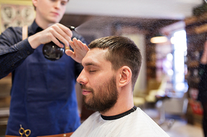 grooming, hairdressing and people concept - hairstylist applying hair styling spray or water to male customer at barbershop