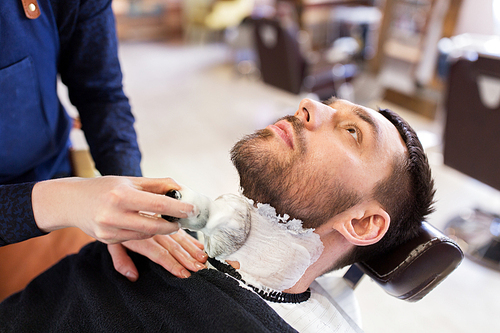 grooming and people concept - man and barber with brush applying shaving foam to beard at barbershop