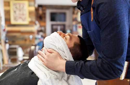 grooming, shaving and people concept - barber softening male face skin with hot towel at barbershop