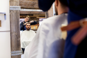 grooming, hairdressing and people concept - man and barber with scissors cutting hair at barbershop