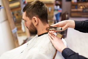 grooming, hairstyle and people concept - man and barber or hairdresser hands with trimmer cutting hair at barbershop