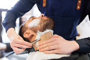 grooming and people concept - man and barber hands with straight razor shaving beard at barbershop