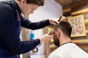 grooming, hairstyle and people concept - man and barber or hairdresser with trimmer cutting hair at barbershop
