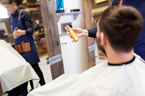 grooming, hairdressing and people concept - hairstylist showing hair styling spray to male customer at barbershop