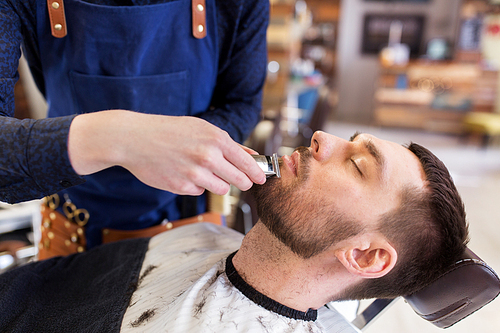 grooming and people concept - man and barber hands with trimmer or shaver cutting beard at barbershop