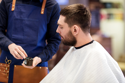 grooming, hairdressing and people concept - hairstylist showing hair styling wax to male customer at barbershop