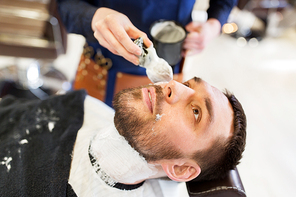 grooming and people concept - man and barber with brush applying shaving foam to beard at barbershop