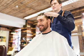 grooming, hairdressing and people concept - man and barber styling hair at barbershop