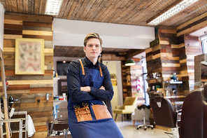 profession, grooming and people concept - male stylist or hairdresser with scissors in apron at hair salon or barbershop