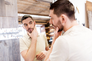 grooming and people concept - man looking at himself at barbershop mirror