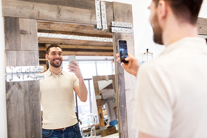 grooming, technology and people concept - happy smiling man with smartphone taking mirror selfie at barbershop or hairdressing salon