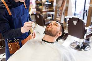 grooming and people concept - hairstylist cleaning client's face and beard with brush at barbershop