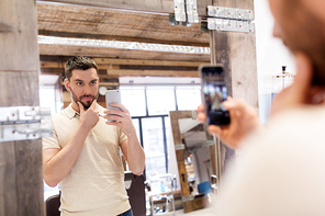 grooming, technology and people concept - man with smartphone taking mirror selfie at barbershop or hairdressing salon and posing