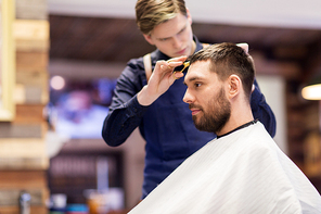 grooming, hairdressing and people concept - man and barber with comb and scissors cutting hair at barbershop