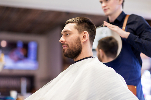 grooming, hairstyle and people concept - man and hairstylist or hairdresser with mirror at barbershop