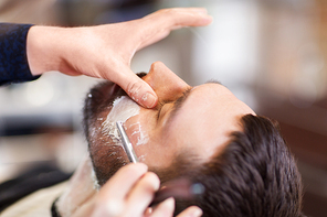 grooming and people concept - man and barber hands with straight razor shaving beard at barbershop