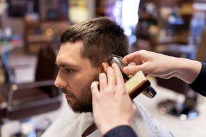grooming, hairstyle and people concept - man and barber or hairdresser hands with trimmer cutting hair at barbershop