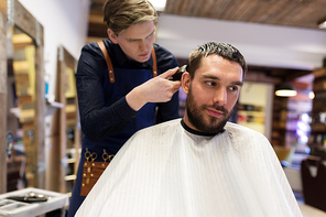 grooming, hairstyle and people concept - man and barber or hairdresser with trimmer cutting hair at barbershop